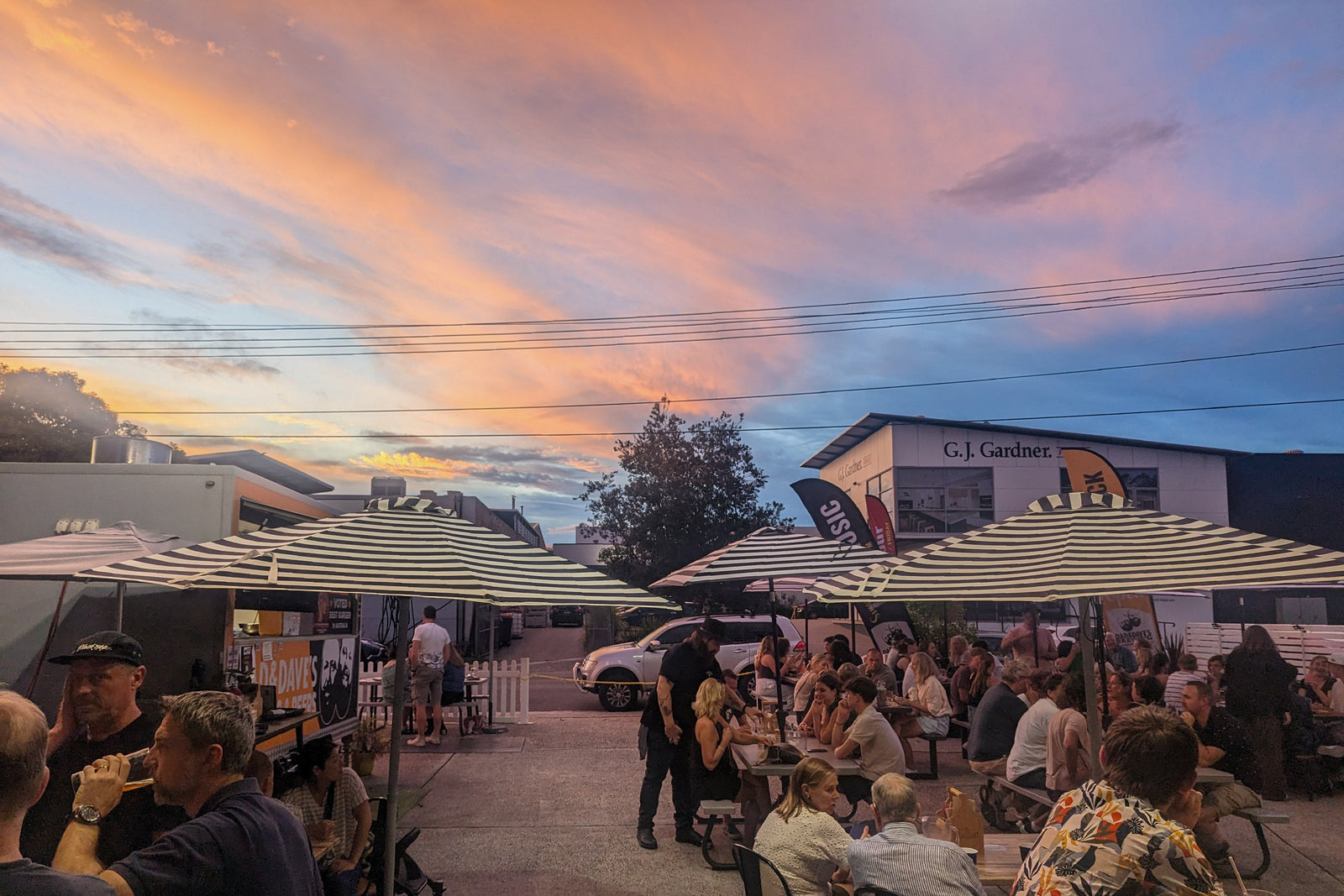 People enjoying outdoor seating at a restaurant with a colorful sunset sky.